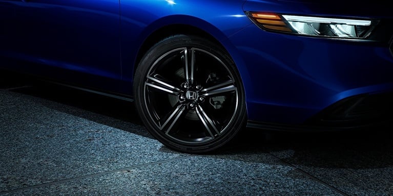 Detail of 2026 Honda Accord in Still Night Pearl in minimalistic urban courtyard environment at night, showing the Sport 19-inch alloy wheels.